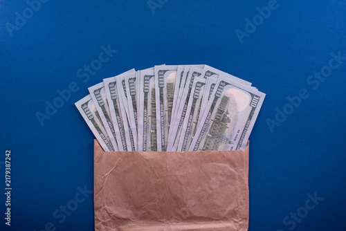 Bild auf Leinwand Fan of 100 US Dollar banknotes emerging from a brown craft envelope on a blue ba
