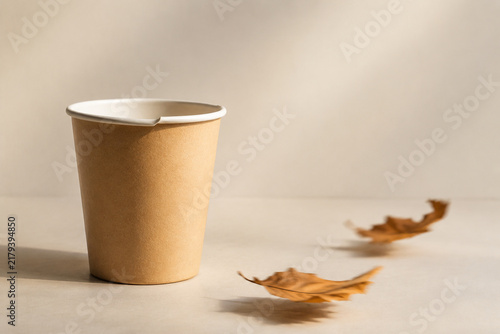 Disposable paper cup with deformed rim and dried autumn leaves in soft breeze, bright studio