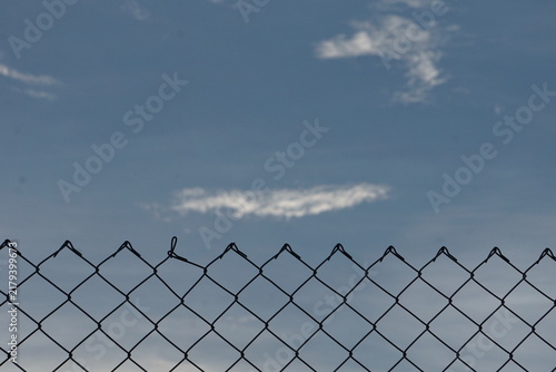 Foto top edge of a chain-link fence cutting horizontally across a serene blue sky with scattered clouds