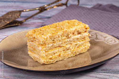 Fotografie Slice of layered napoleon cake on ceramic plate with golden crust and cream fill