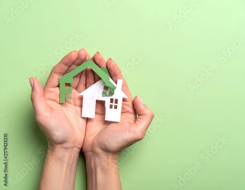Two hands cradle a paper house with a green roof against a light green backdrop