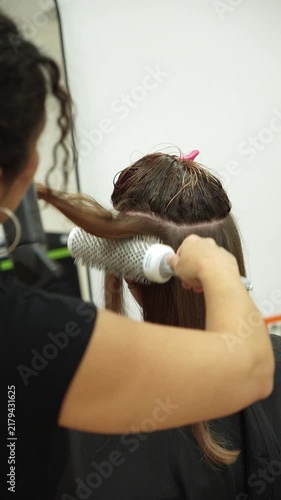 Hairdresser dries wet hair with a blow dryer and round brush in a beauty salon. Professional styling scene for hair care, grooming, beauty services and salon marketing