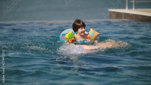 Happy Little Boy Swimming with Inflatable Ring in Pool as Mother Dives Under Water