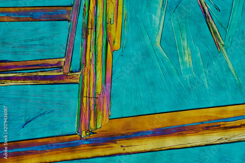 Polarized light microscopy of magnesium sulfate crystal ladder pattern with vibrant cyan background and golden prismatic columns