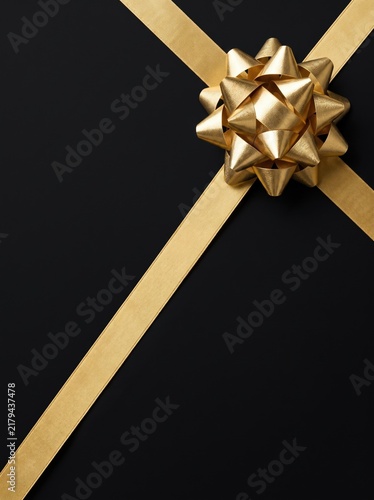A gold ribbon bow crosses over itself, isolated on a plain black background, ready for gift wrapping design.