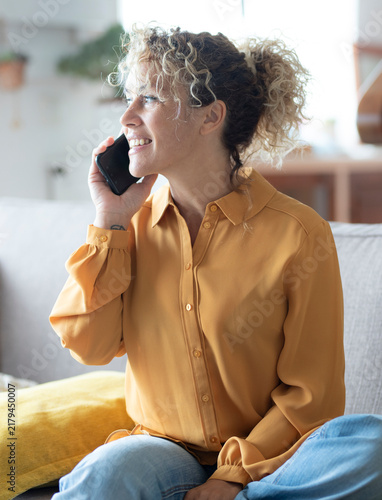 Cuadro en lienzo Woman with curly hair smiling and talking on a smartphone while sitting comforta