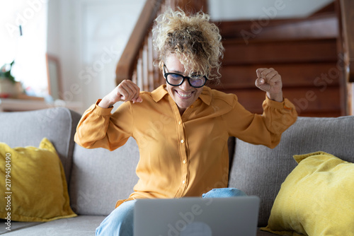 Фотография Woman feeling happy and celebrating success, looking at her laptop while sitting