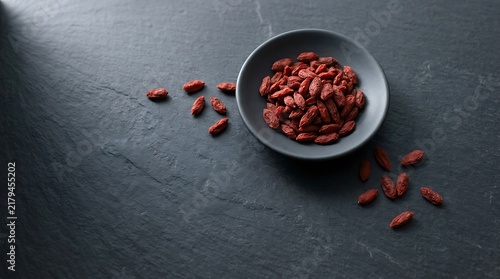 Goji berries top view in a black bowl on a dark slate surface, healthy dried superfood concept