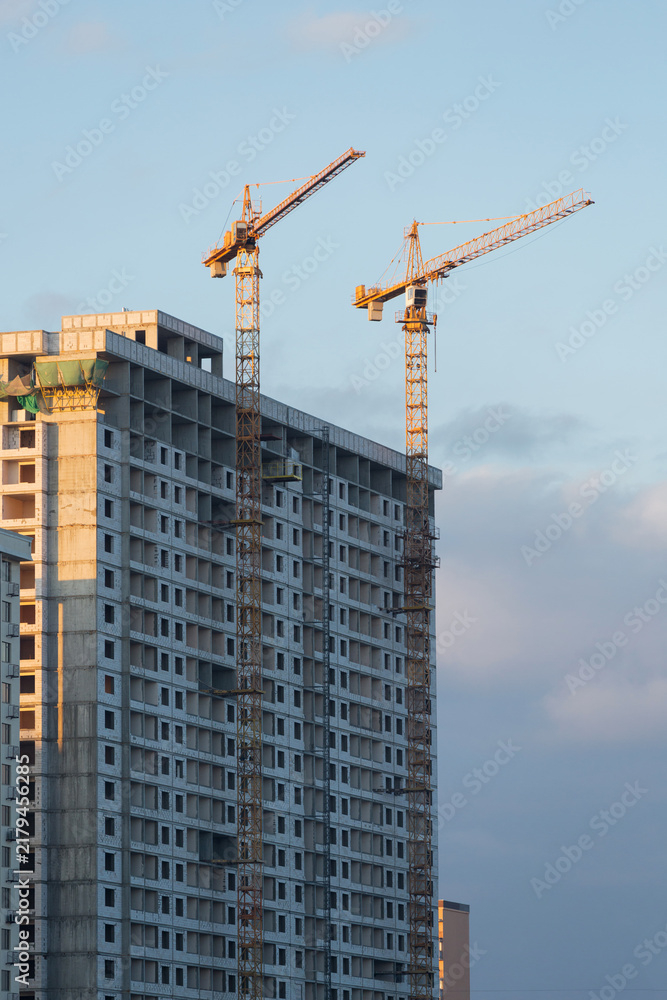 Fototapeta premium Yellow tower cranes constructing modern high rise residential building at sunset