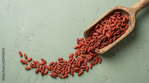 Goji berries top view in a wooden scoop on a green textured surface, healthy superfood flat lay food photography