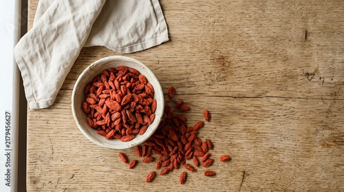 Goji berries top view in white ceramic bowl on rustic wooden table with cloth napkin next to spilled dried fruit