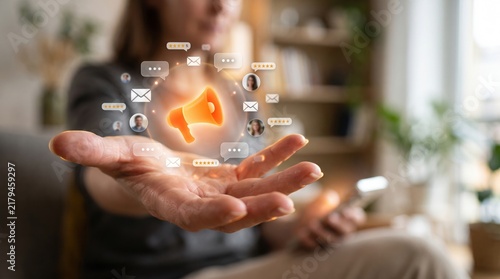 A hand holding a glowing megaphone icon surrounded by digital communication symbols, representing marketing and promotion.