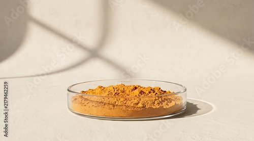 A petri dish filled with vibrant orange pumpkin powder on a neutral beige background with natural light shadows