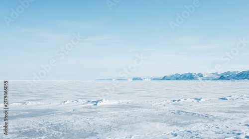 A wide, expansive view of a bright, icy landscape. A vast, flat expanse of white snow and ice stretches out to the horizon.