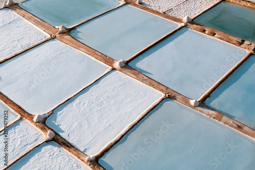 aerial view of traditional sea salt evaporation ponds with geometric patterns, crystallized salt beds and turquoise brine pools in coastal saltworks