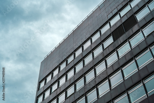 Low angle perspective of a dark modern office building facade with glass windows under a cloudy sky