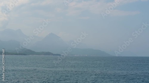 Calm seascape with distant misty mountains across tranquil blue water under a cloudy sky. Peaceful coastal landscape with atmospheric haze, natural scenery, scenic marine horizon. Ideal for travel
