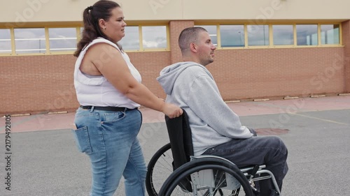 Manual wheelchair user enjoying an outdoor stroll with a Personal assistant while chatting, smiling, and spending quality time together.