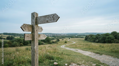 Weathered signpost with four arms on a grassy hill above a wide valley