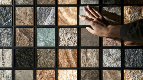 A hand touches a marble tile sample on a showroom wall.