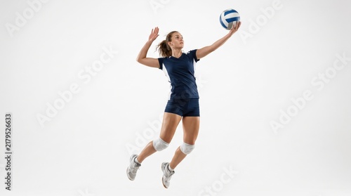 Full length studio shot of a young adult caucasian female volleyball player jumping and hitting the ball, isolated on white background for sports advertising concepts