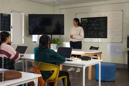 Diverse students and Indian presenter discussing code on screen with laptops in class, copy space