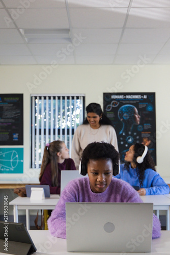 Indian teacher guiding teen girls in class, African American student in purple sweater using laptop