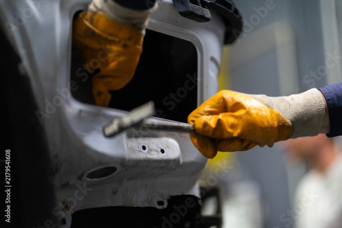 Worker hands in gloves repair damage on car body at service station closeup. Professional mechanic fixes automobile frame in workshop