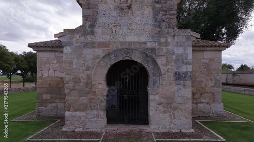 Aerial drone pull-back shot from horseshoe arch porch revealing the 7th-century Visigothic Church of San Juan de Baños in Palencia, Spain.