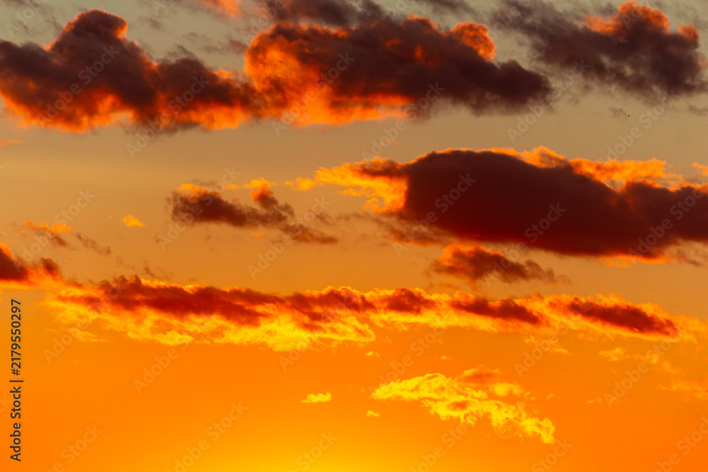 Fototapeta premium Fiery orange clouds glowing against a golden sunset sky, dramatic atmospheric light creating a vibrant celestial canvas with intense warm hues during the magical golden hour