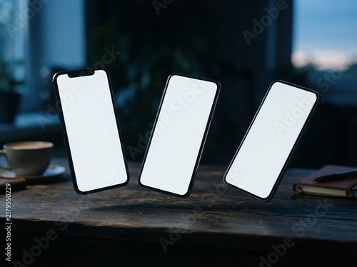 Three phones with blank screens floating above a dark wooden city desk