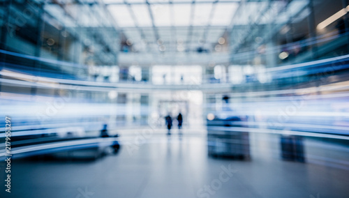 Abstract blurred motion background of a modern corporate office atrium with dynamic light streaks and indistinct silhouettes, representing fast-paced business and future technology.