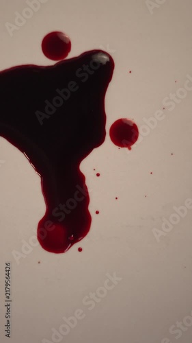 Blood dripping into viscous pool on neutral background for thriller crime scene, top view zoom in slow motion, bottom copy space, vertical video
