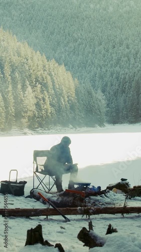 Man camping and cooking on a frozen lake shore