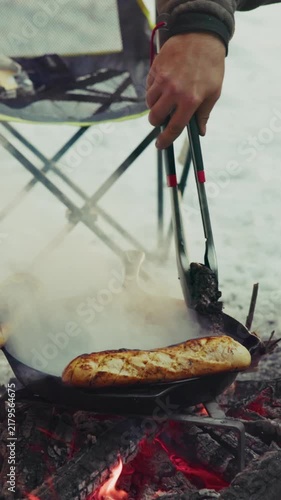 Hiker cooking baguette bread on campfire in winter snow