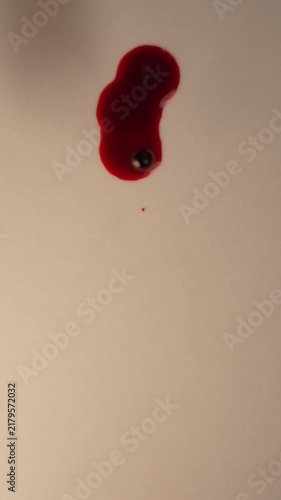 Fresh blood drop falling onto empty cream background for forensic evidence, top view close up slow motion, bottom copy space, vertical video