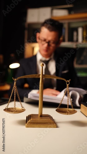 Brass scale of justice on desk with blurred lawyer holding hand on forehead in deep thought