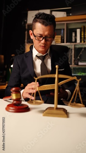 Asian Lawyer Reading Law Book Behind Brass Scales of Justice and Wooden Gavel