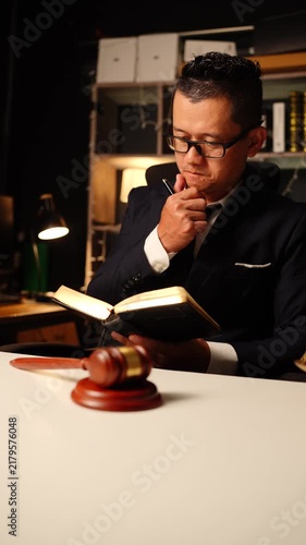 Lawyer reading and writing in law book sitting behind wooden judge gavel