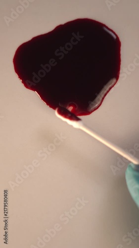 Forensic swab swabbing blood pool for crime scene investigation and lab analysis, top view slow zoom in, blue gloved hand, bottom copy space, vertical video