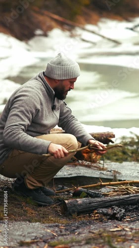 Hiker preparing campfire by a frozen lake in winter
