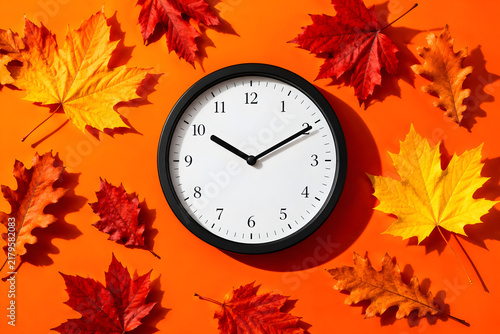 Autumn daylight savings time clock, fall leaves on orange background, seasonal time change concept for winter schedule