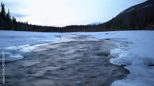 A Serene Winter Landscape with Snow-Covered Banks and a Partially Frozen River Under a Clear Blue Sky