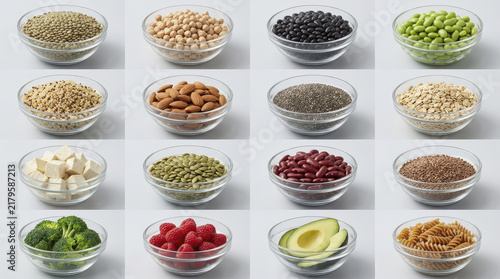 Variety of high protein and high fiber foods are displayed in glass bowls including beans, nuts, seeds, tofu, and vegetables