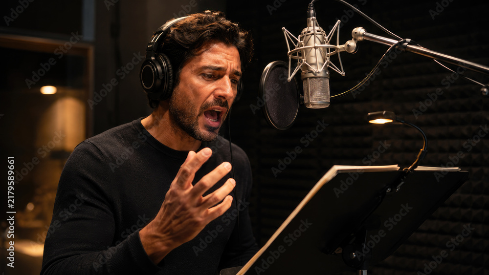 Obraz premium Man performing an emotional voiceover in a professional recording studio booth, reading from a script into a microphone