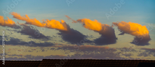 Row of bizarre sunlit clouds at sunset over roof