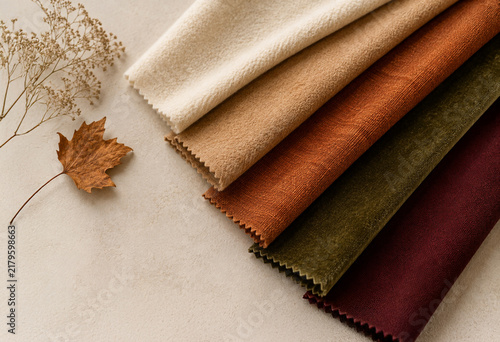 Elegant fabric swatches in cream, beige, terracotta, olive green and burgundy arranged on a neutral background with a dried autumn leaf. Warm seasonal textile color palette with copy space.