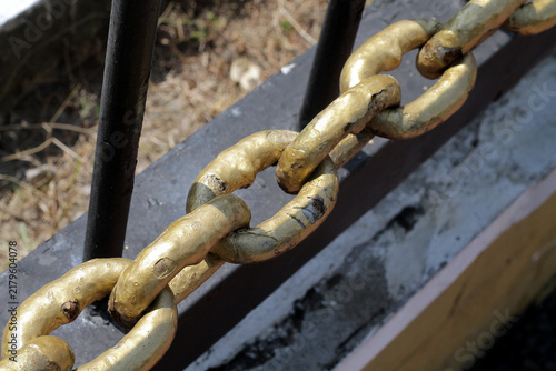 Close-Up of Weathered Gold Metal Chain Links on Outdoor Barrier Railing Showing Texture and Strength