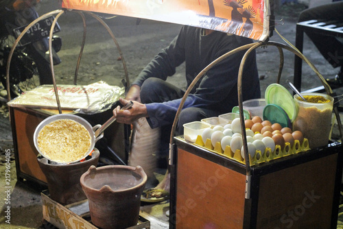 Street Food Vendor Frying Eggs at Night Market Cart With Charcoal Stove and Pan
