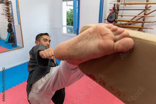 Fotografía Man in martial arts uniform kicking a wooden board during hapkido training, focu